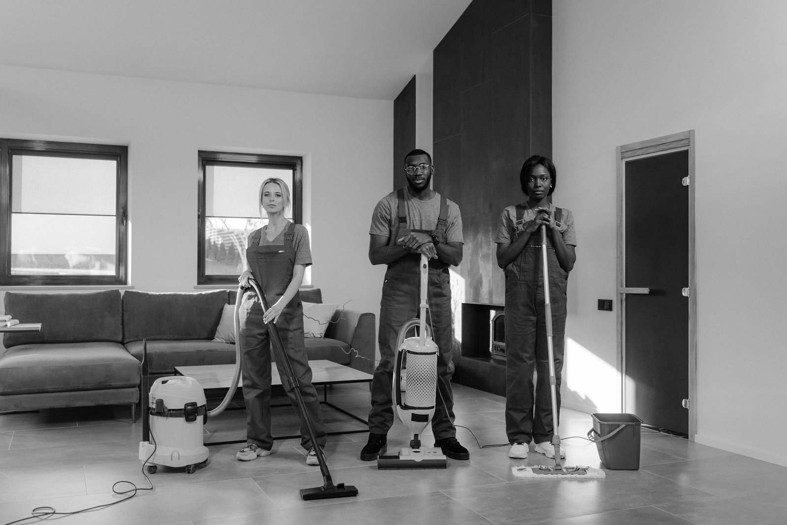 A team of three professional cleaners in uniforms with equipment ready for housekeeping.