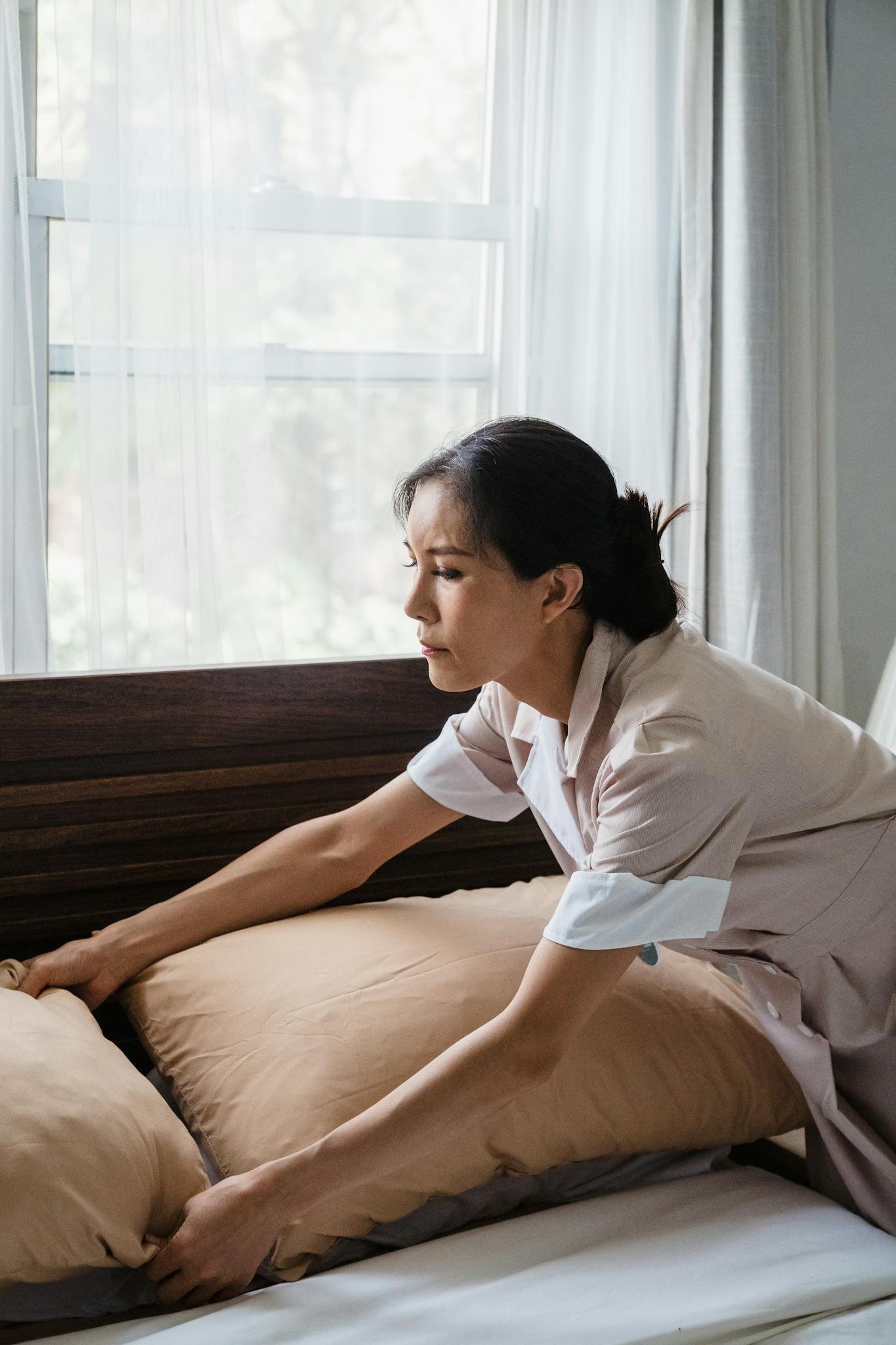 A dedicated housekeeper tidying a hotel bed, enhancing room comfort.
